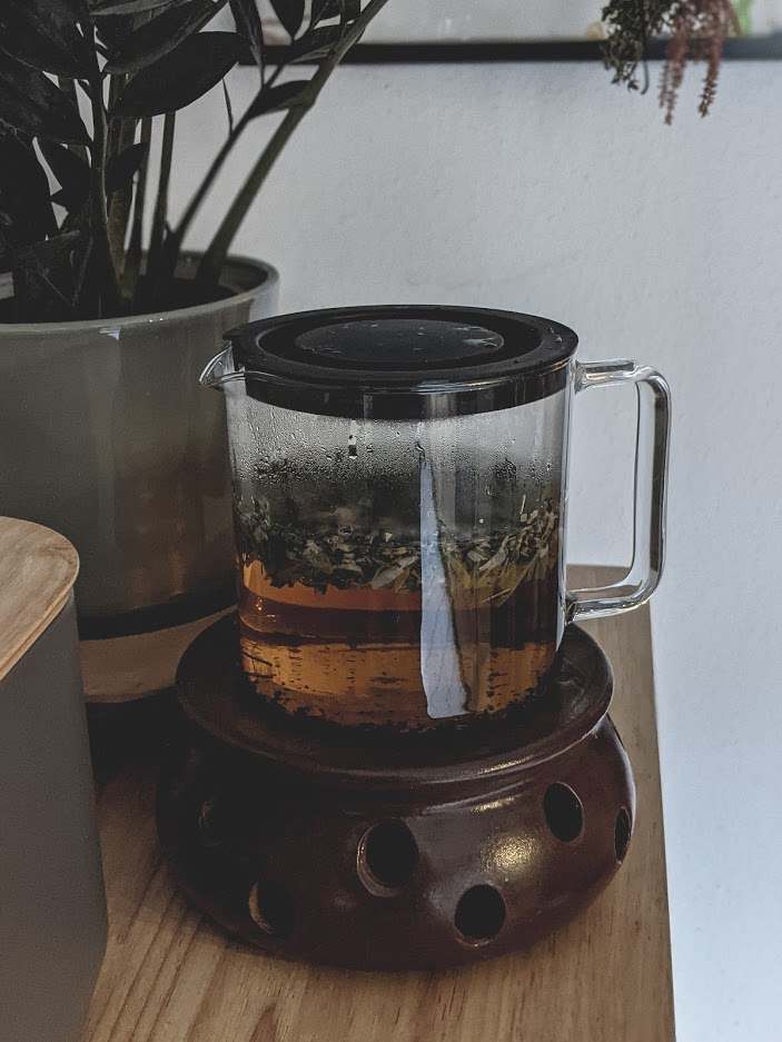 Haar-Tee in Glaskanne auf einem braunen Stövchen